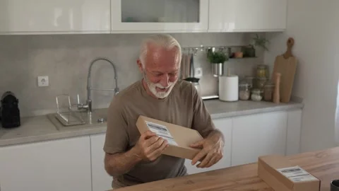 Senior man sit at home hold post package delivery present or order Stock Footage 250296450