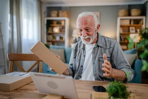 Senior man sit at home hold post package delivery use digital tablet Stock Photos