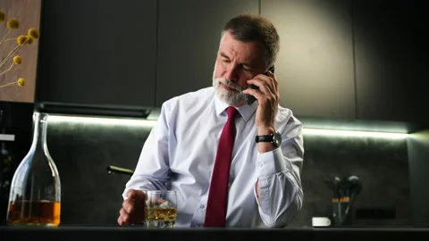 Senior man sit in kitchen drinking whiskey talking on smartphone Stock Footage 234651137