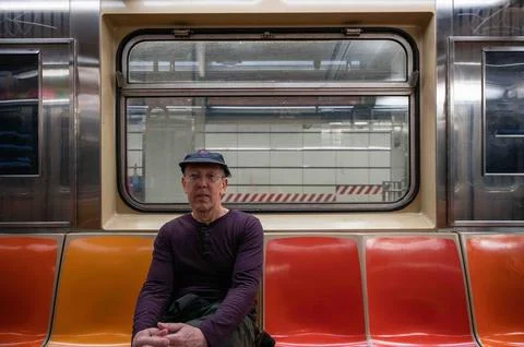 Senior man sits alone on an empty subway car stopped at a station Stock Photos