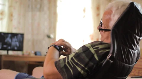 Senior man sits with smart clock in a leather chair near the house TV. A man Stock Footage 65080313