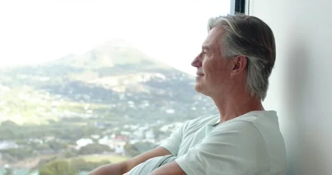 Senior man sitting by big window hills drawing gaze wearing light tee finding Stock Footage 339415357