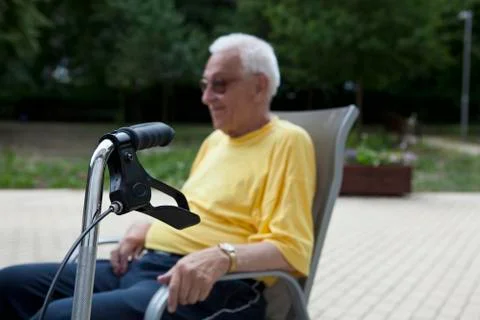 A senior man sitting in a chair, the handle of his walker in the foreground, Stock Photos