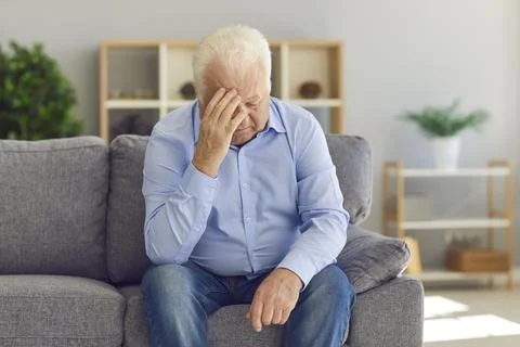 Senior man sitting on couch, grieving over loss of wife, or suffering from bad Stock Photos