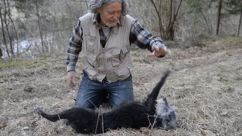 Senior man sitting on the floor by the river playing with his black dog Stock Footage 104860274