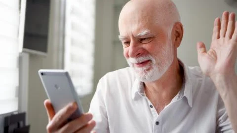 Senior man sitting at home with smartphone. Using mobile talking via messenge Stock Photos