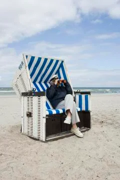 A senior man sitting in a hooded beach chair looking through binoculars Stock Photos