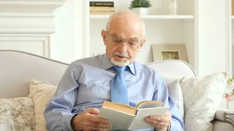 Senior man sitting on the sofa and reading a book Stock-Footage 89035041