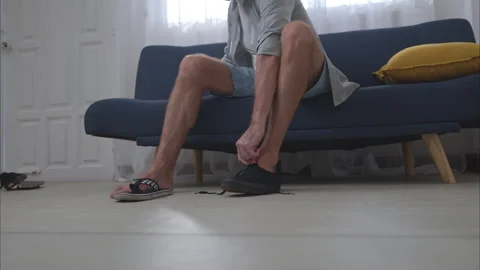 Senior man sitting on a sofa choosing between different pairs of shoes Stock Footage 326179951