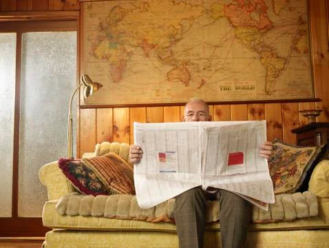 Senior Man Sitting On Sofa Reading Newspaper Stock Photos
