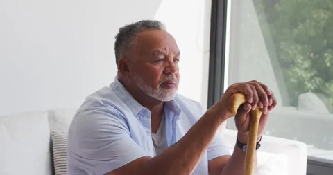 Senior man sitting on sofa by window, gazing out, holding cane, turning, Stock Footage 340974669