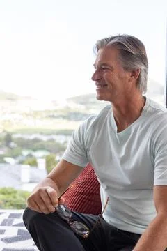 Senior man sitting on sofa by window looking at hills holding tortoiseshell Stock Photos
