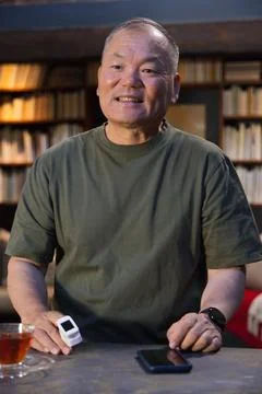 Senior man sitting at table in study, wearing olive tee, holding fingertip Foto stock