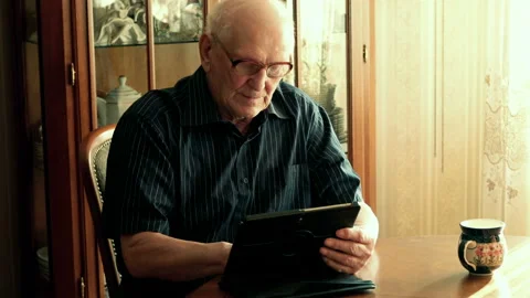 Senior man sitting with tablet by table, at home, 4K Stock Footage 105295267