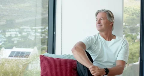 Senior man sitting on window bench, noticing hillside view and contemplating, Stock Footage 341736517