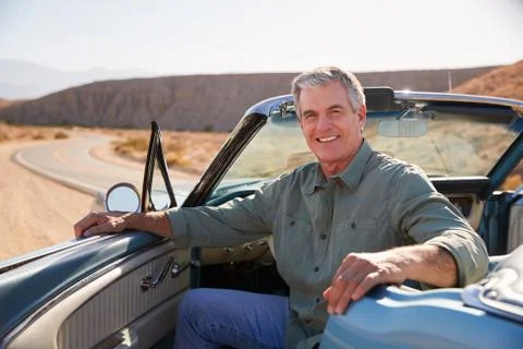 Senior man smiling to camera from parked open top car Fotos Stock