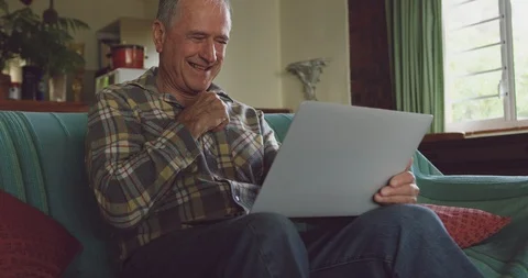 Senior man smiling while using laptop at home 스톡 동영상 122904584