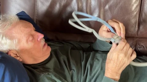 Senior man on sofa adjusts his CPAP Stock Footage 310640670