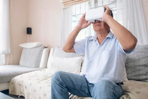 Senior man on sofa couch using VR headset at home. Stock Photos