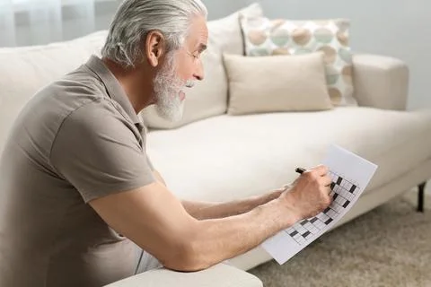 Senior man solving crossword on sofa at home Stock Photos