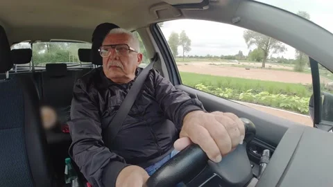 Senior man with spectacles drives car along road past garden Stock-Footage 140966992