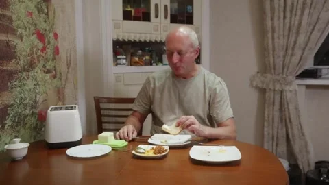 Senior man spreading butter on bread at kitchen table Vidéo 324907823