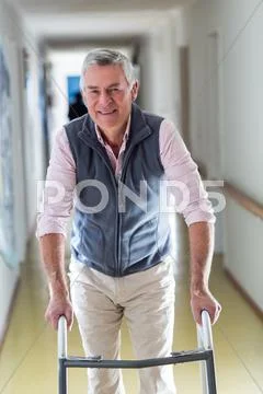 Senior Man Standing In Hospital Corridor With Walking Frame