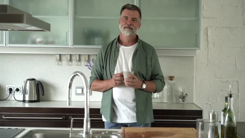Senior man standing in kitchen drinking mug of coffee, spending time alone Stock Footage 189800008
