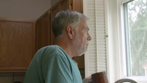 Senior man standing next to a kitchen window drinking coffee Video stock 202088599