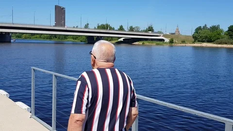 Senior man stands on pier talking on phone at tranquil river Stock Footage 112395328