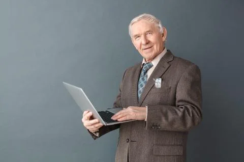 Senior man studio standing isolated on gray typing message on laptop smiling Stock Photos