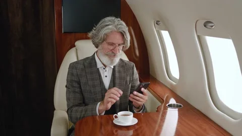 Senior man in suit using smartphone while flying in private airplane. Stylish Stock Footage 198082186