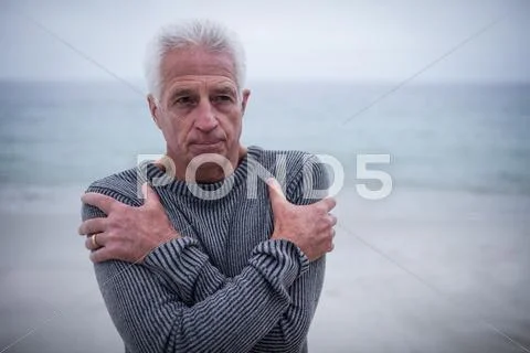 Senior Man In Sweater Feeling Cold On The Beach