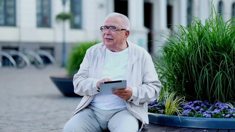 Senior man with tablet sits at flowerbed on city square Stock Footage 115883875