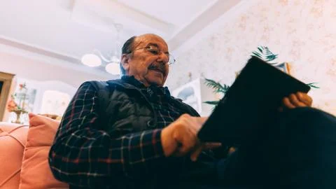 Senior man with tablet sitting on sofa at home. Stock Photos
