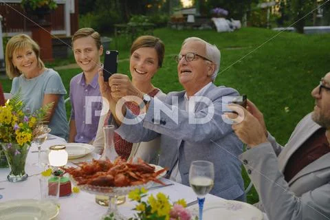 Senior man taking selfie with family at summer garden party dinner Stock Photos