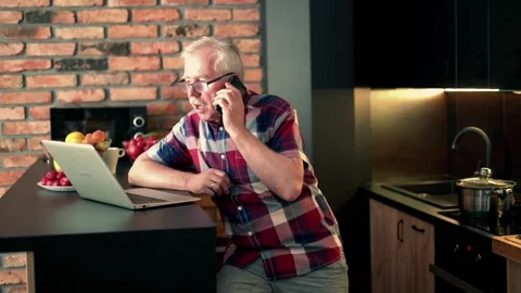Senior man talking on cellphone and using laptop at home Stock Footage 108456776