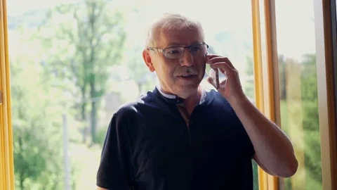Senior man talking on cellphone by window with country view Stock Footage 80890435