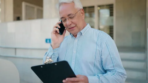 Senior man talking on the smartphone reading document at street Video stock 201759242