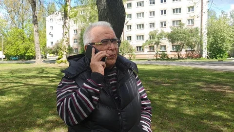 Senior man talks on mobile phone in sunny spring park Stock Footage 112416331