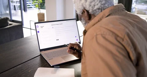 Senior man tapping laptop clearing chat, writing proposal in notebook at desk, Stock Footage 314029725