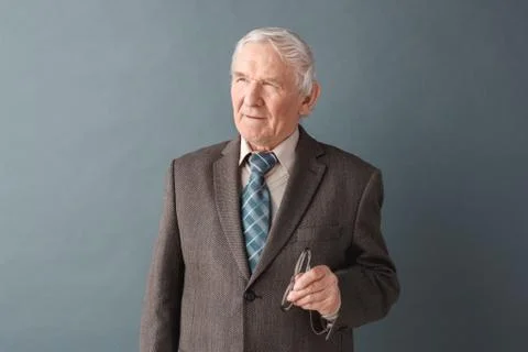 Senior man teacher studio standing isolated on gray holding glasses thoughtful Stock Photos