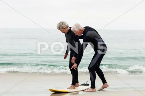 Senior man teaching woman to surf on beach Stock Photos