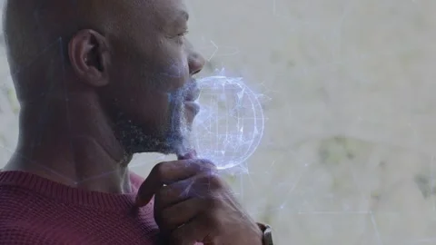 Senior man touching chin by window making holo sphere beside mouth growing net Stock Footage 333485867