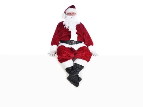 Senior man in traditional Santa Claus Suit sitting on a white wall.  Isolated Stock Photos