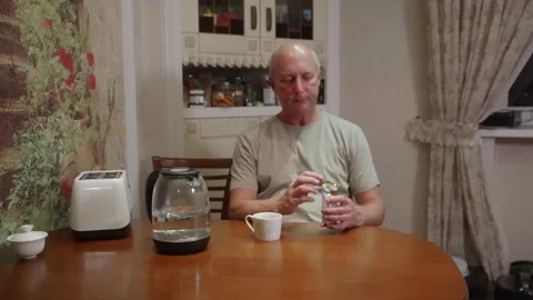 Senior man unwrapping chocolate at kitchen table, everyday snack Stock Footage 324907856
