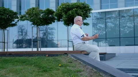 Senior man uses tablet on bench at modern office center Stock Footage 115884550