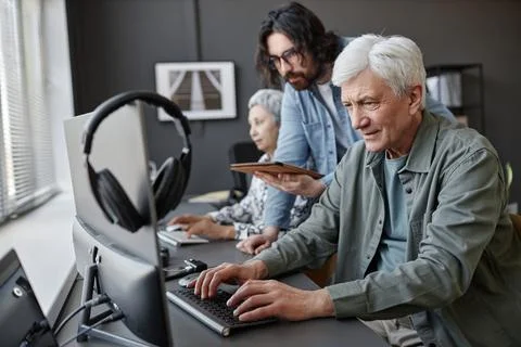Senior man using computer in class with male instructor helping Stock Photos