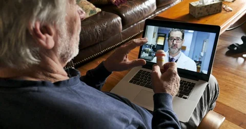 Senior man using a computer for a telemedicine appointment with his doctor Stock Footage 120292582