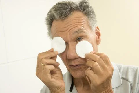 Senior man using cotton pads for eye relief Stock Photos
